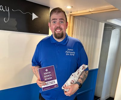James Gardiner owner of James Patisserie in Honiton with bottle of champage and Honiton Business Network flyer.